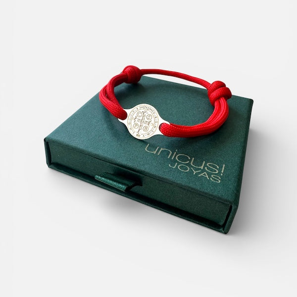 Pulsera cruz san benito plata con diseño sagrado sobre caja de joyería verde.