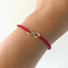 Pulsera infinito de macramé con hilo rojo y charm de plata en una muñeca.
