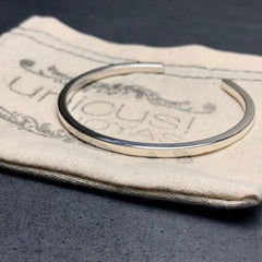 Esclava de plata maciza sobre una bolsa de tela, destacando su acabado pulido espejo.